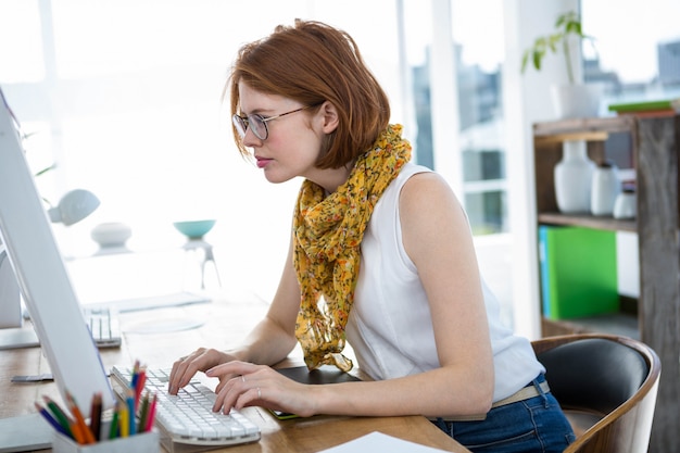 doordachte hipster zakenvrouw, zittend aan haar bureau, zich te concentreren op haar computer