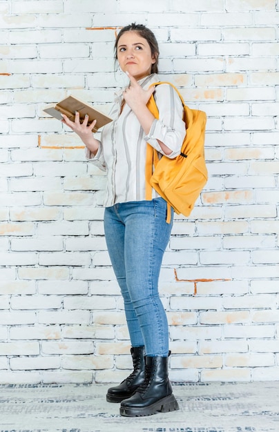 Doordachte jonge dame die een boek vasthoudt en denkt Foto van hoge kwaliteit