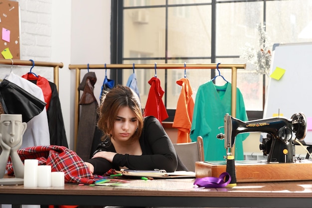 Doordachte jonge kleermaker zit in het atelier en kijkt opzij