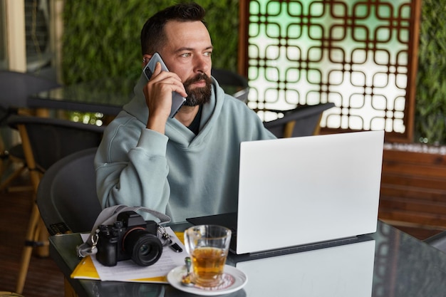 Doordachte jonge volwassen man in casual kleding in café praten op een mobiele telefoon