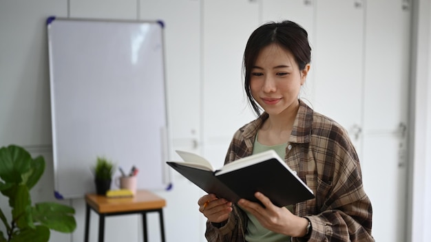 Doordachte jonge vrouw die een boek leest terwijl ze op een moderne werkplek zit