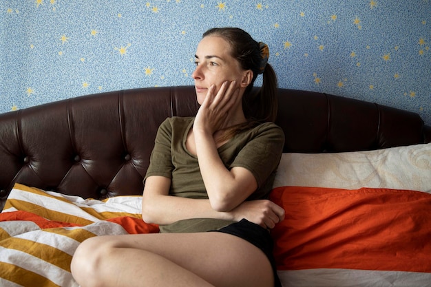 Doordachte jonge vrouw die wegkijkt terwijl ze op bed in de slaapkamer zit