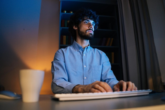 Doordachte jonge zakenman die 's avonds laat op het kantoor aan huis op de computer werkt