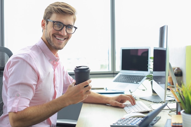 Doordachte jonge zakenman in shirt die met behulp van de computer werkt terwijl hij op kantoor zit.