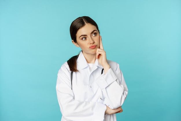 Doordachte medische werker jonge doktersvrouw die er ongeamuseerd verveeld uitziet in witte jas tegen b...