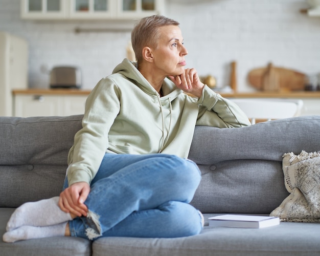 Doordachte mooie vrouw van middelbare leeftijd in vrijetijdskleding dromen en denken in haar bank