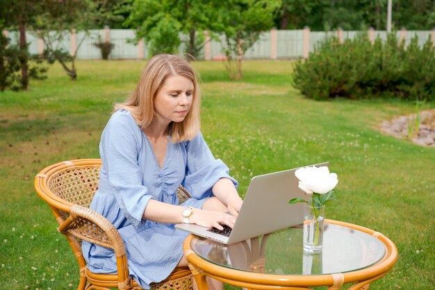 Doordachte schattige vrouw die met haar laptop aan tafel in park of tuin werkt