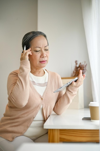 Doordachte senior Aziatische vrouw die haar tablet gebruikt terwijl ze ontspant in een coffeeshop