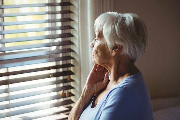 Doordachte senior vrouw kijkt uit raam thuis