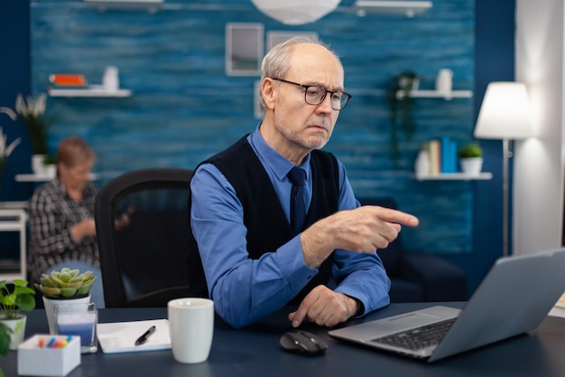 Doordachte senior zakenman wijzend op laptop terwijl hij thuis werkt working