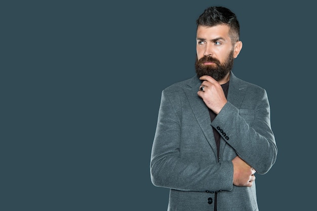 Doordachte volwassen man met baard draagt casual op grijze achtergrond