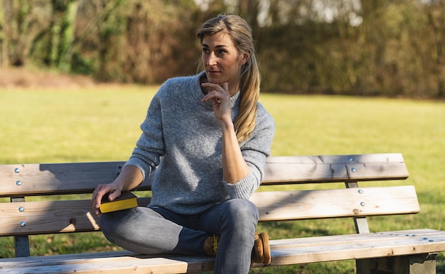 Doordachte vrouw zittend in het park op een bankje student denken met een boek in het park concept afbeelding