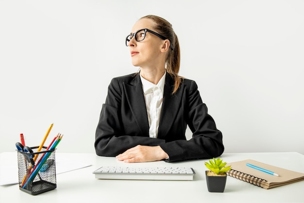 Doordachte zakenvrouw in een jas met bril zittend aan een bureau op kantoor