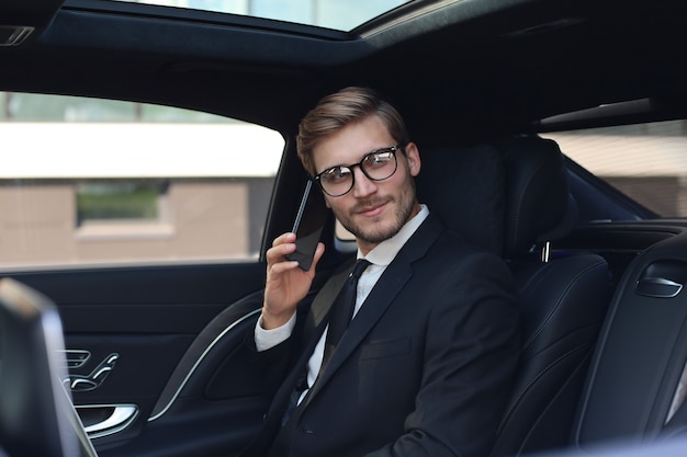 Doordachte zelfverzekerde zakenman die aan de telefoon praat terwijl hij in de auto zit.