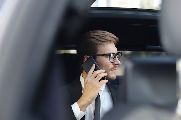 Doordachte zelfverzekerde zakenman die aan de telefoon praat terwijl hij in de auto zit.