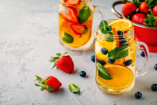 Doordrenkt detoxwater met oranje bosbes, aardbei en munt IJskoude zomercocktail of limonade in glazen glazen pot