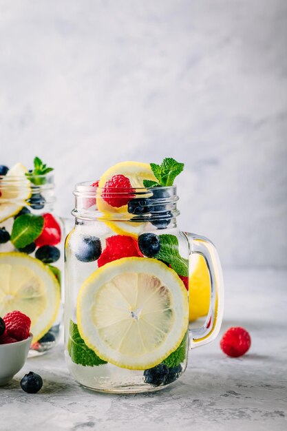 Doordrenkt detoxwater met schijfje citroen, framboos, bosbes en munt IJskoude zomercocktail of limonade in glazen glazen pot