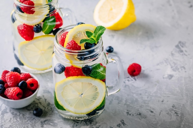 Doordrenkt detoxwater met schijfje citroen, framboos, bosbes en munt IJskoude zomercocktail of limonade in glazen glazen pot