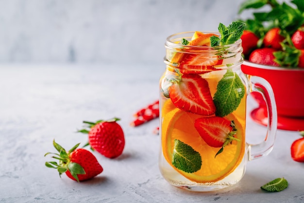 Doordrenkt detoxwater met sinaasappelaardbei en munt IJskoude zomercocktail of limonade in glazen glazen pot