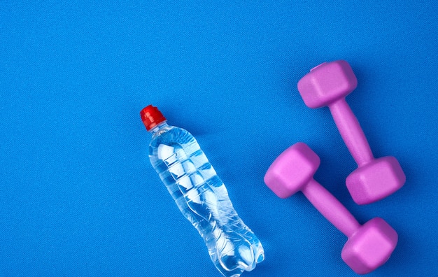 Doorzichtige plastic fles water en een paar paarse plastic dumbbells