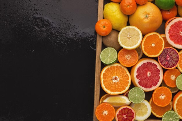 Doos met assortiment van citrusvruchten op natte zwarte achtergrond, kopieer ruimte. Bovenaanzicht op sinaasappelen, citroenen, mandarijnen en ander exotisch fruit, plat gelegd. Het maken van detox freshes concept en recept mockup