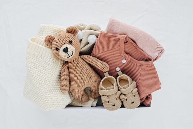 Doos met babyspullen en accessoires voor pasgeborenen op bed. Geschenkdoos met gebreide deken, kleding, sokken, schoenen en speelgoed. Babydouche-concept. Platliggend, bovenaanzicht