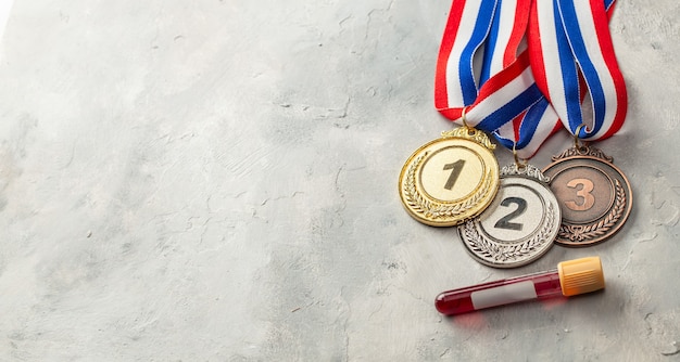 Dopingtest. Gouden, zilveren en bronzen medaille en reageerbuis met bloed op een grijze achtergrond.