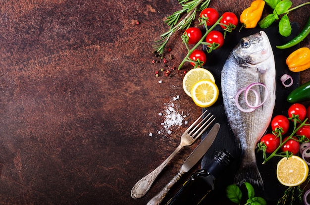 Dorada, fresh fish with vegetable, lemon, herbs, onion, paprika, cherry tomatoes, onion, salton dark vintage background. 