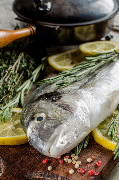 Dorado fish with lemon thyme rosemary and spices Wooden kitchen Board Pepper Vintage pan