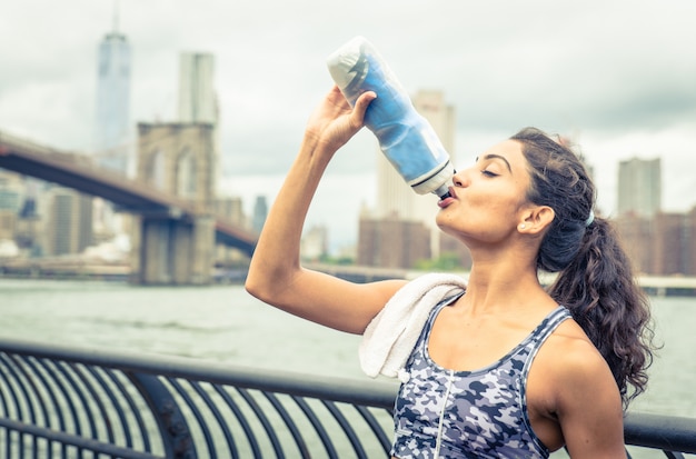 Dorstige atleet drinken na lange termijn in de stad van New York. Brooklyn bridge en skyline op de achtergrond