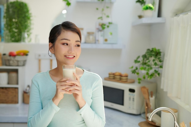 Dorstige jonge vrouw die melk drinkt uit een glas in de keuken