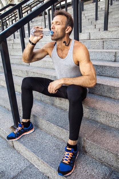 Dorstige sportman rust uit en drinkt water na het hardlopen. fitness, sport, sporten en mensen gezonde levensstijl concept.