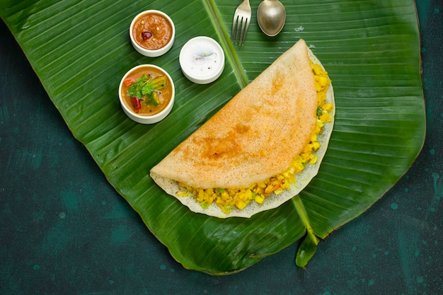 Dosa Masala dosafamous 남부 인도식 아침 식사 항목은 전통적인 방식으로 철판으로 만들어지고 짙은 녹색 배경이 분리된 신선한 바나나 잎에 배열됩니다.