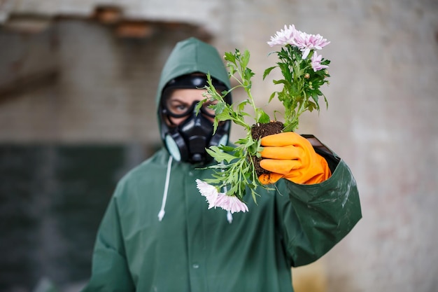 A dosimetrist scientist radiation inspector in protective clothing and a gas mask examines the danger zone Closeup Flower Ecological catastrophy