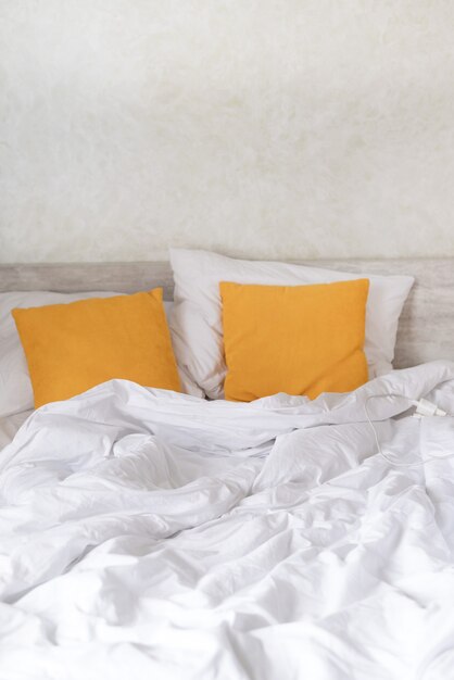 Двуспальная кровать в спальне с декоративными желтыми подушками и скомканная кровать