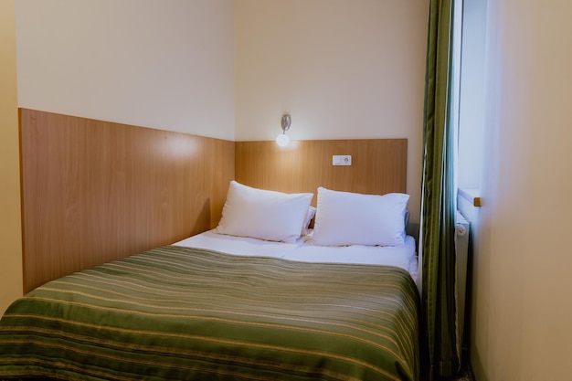 Двуспальная кровать в простом и красиво обставленном уютном гостиничном номере в дневное время