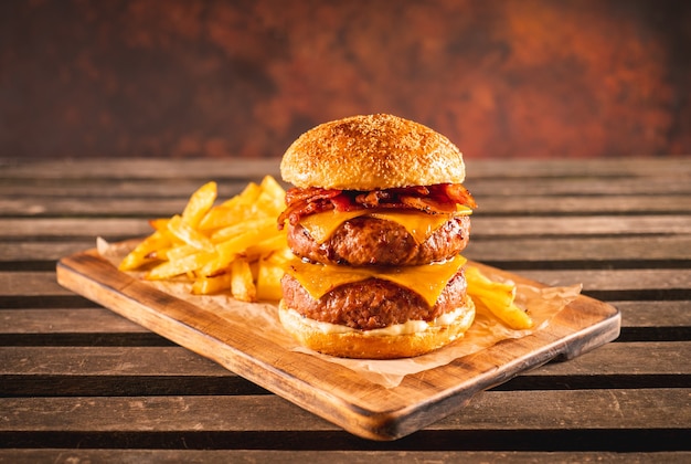 Double beef and bacon burger with cheddar cheese and chips on a\
wooden board