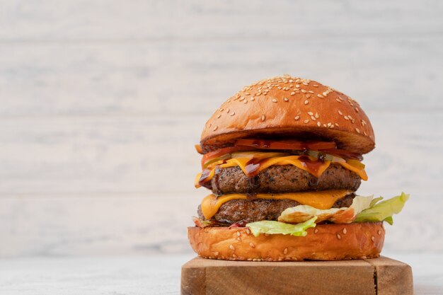 Double cheeseburger served on wooden board against white blurred background