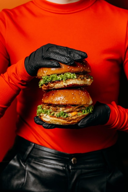 濃い赤い服に黒い手袋で握られたダブルチーズバーガー 印象的な食事コンセプト