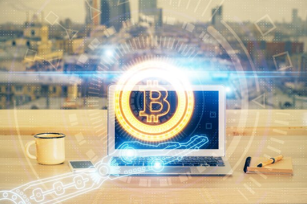 ブロックチェーンと暗号経済テーマのホログラムとコンピューターの背景を持つテーブルの二重露光ビットコイン暗号通貨の概念