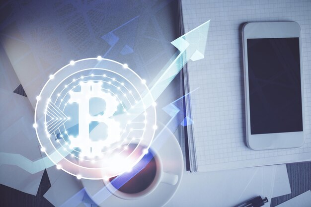 ブロックチェーンテーマのホログラムをテーブルの上で電話で二重露出する トップビュー 暗号技術コンセプト