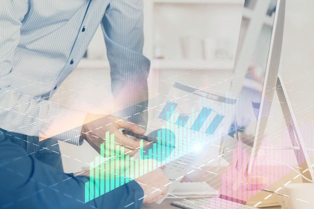 Double exposure of chart with businessman typing on computer in office on background Concept of hard work