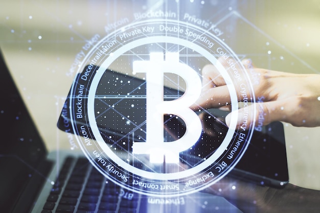 Double exposure of creative Bitcoin symbol hologram and hand working with a digital tablet on background Mining and blockchain concept