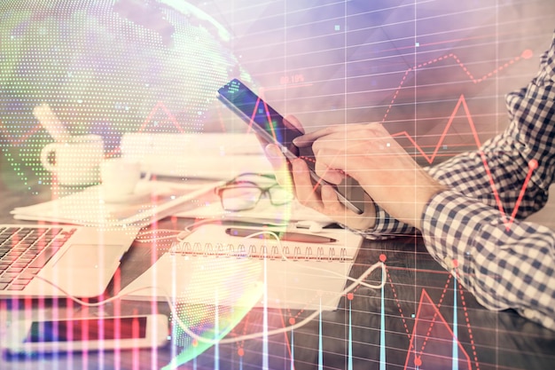 Double exposure of man's hands holding and using a digital device and forex graph drawing Financial market concept