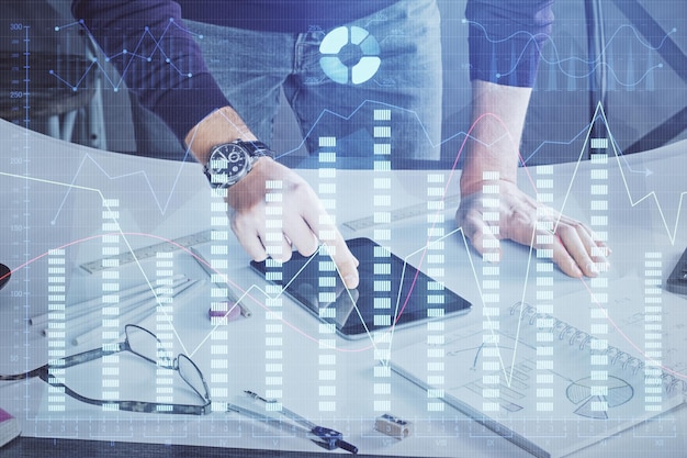 Double exposure of man's hands holding and using a digital device and forex graph drawing Financial market concept