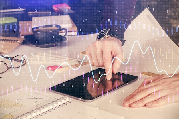 Double exposure of man's hands holding and using a digital device and forex graph drawing Financial market concept