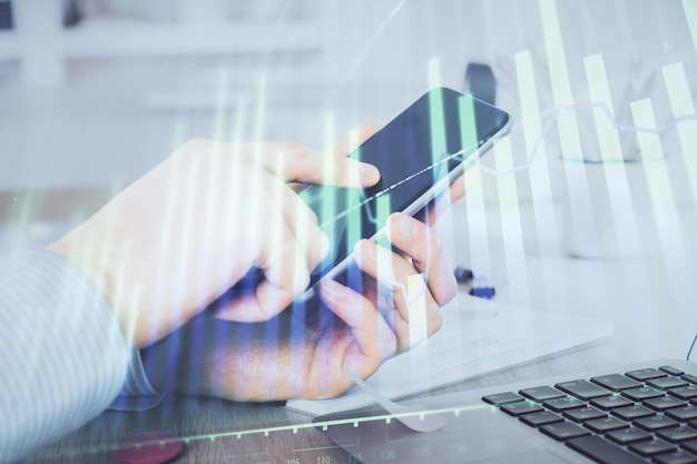 Double exposure of man's hands holding and using a digital device and forex graph drawing Financial market concept