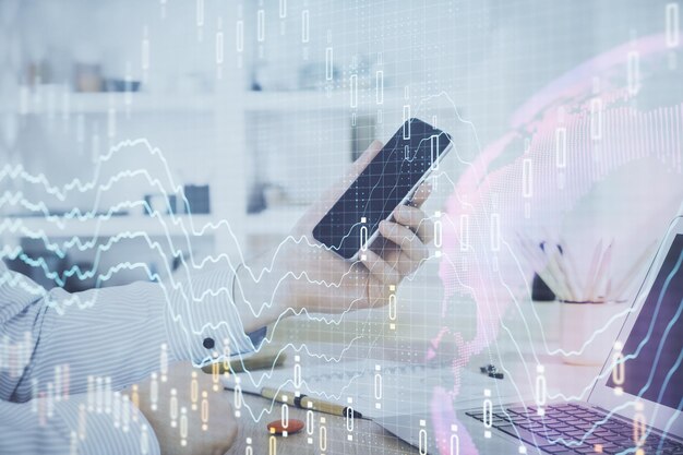 Double exposure of man's hands holding and using a digital device and forex graph drawing Financial market concept