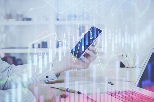 Double exposure of man's hands holding and using a digital device and forex graph drawing Financial market concept