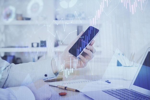 Double exposure of man's hands holding and using a digital device and forex graph drawing Financial market concept